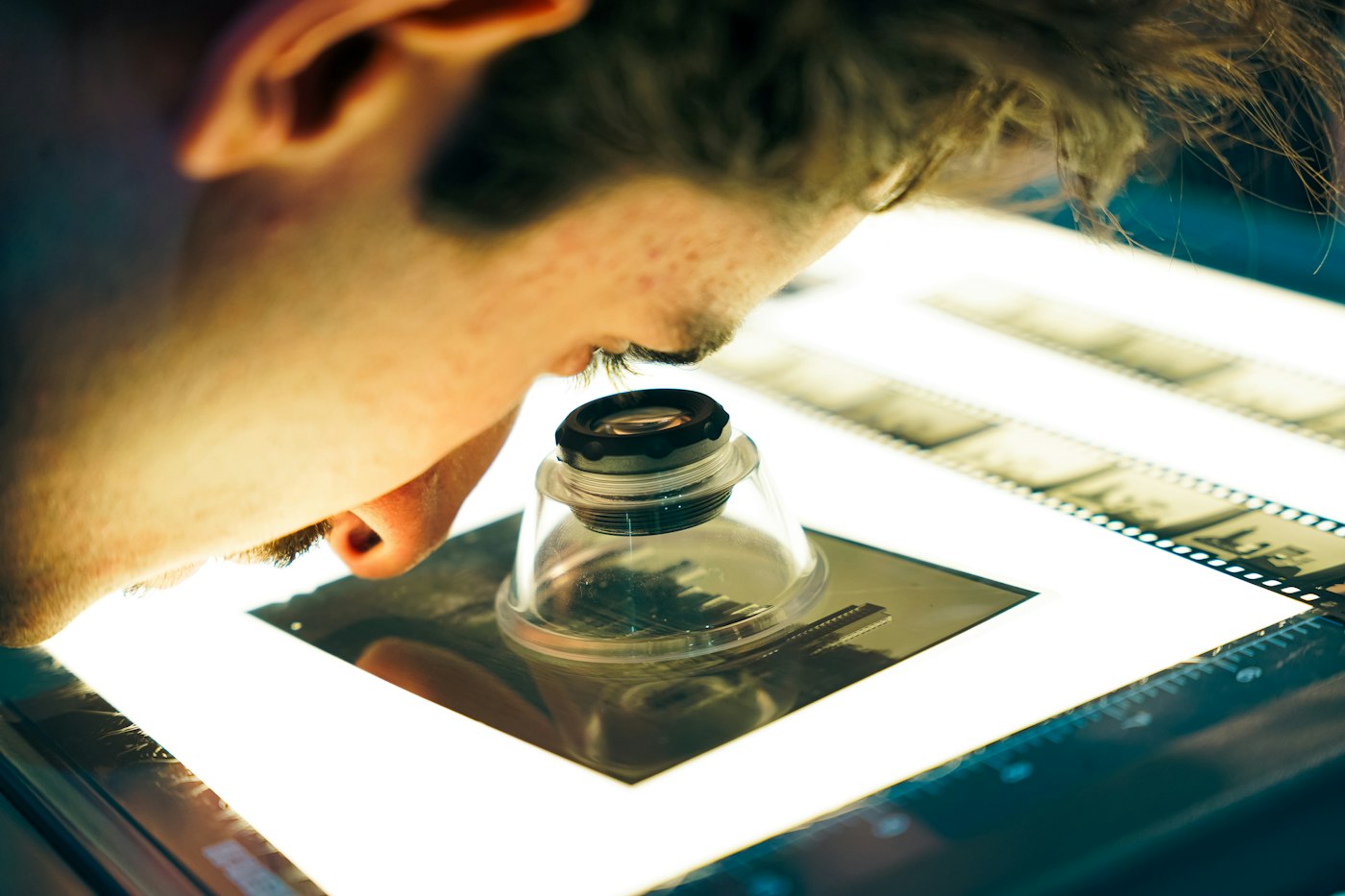 Close-up of a photographer inspecting film negatives with a loupe on a light table