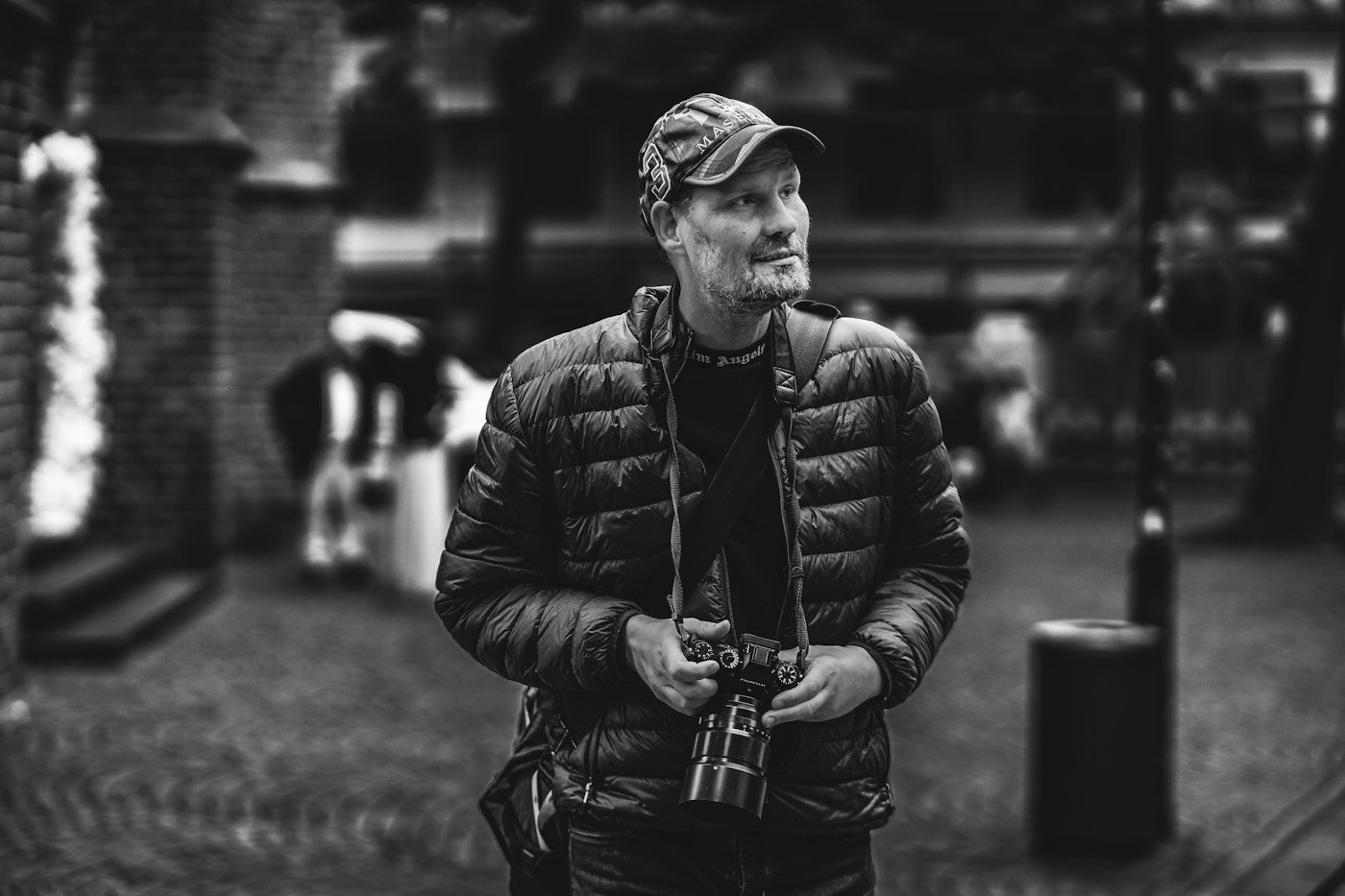 Black-and-white portrait of Iñigo holding a rangefinder camera on a street