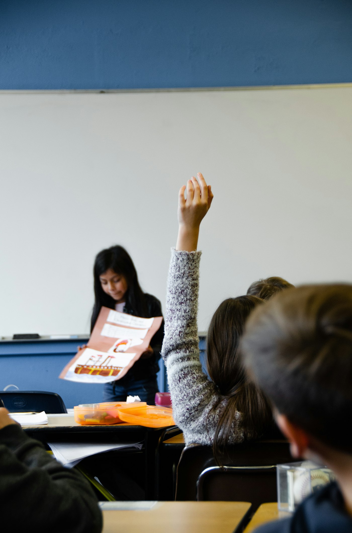 A student raising a hand in a bright classroom