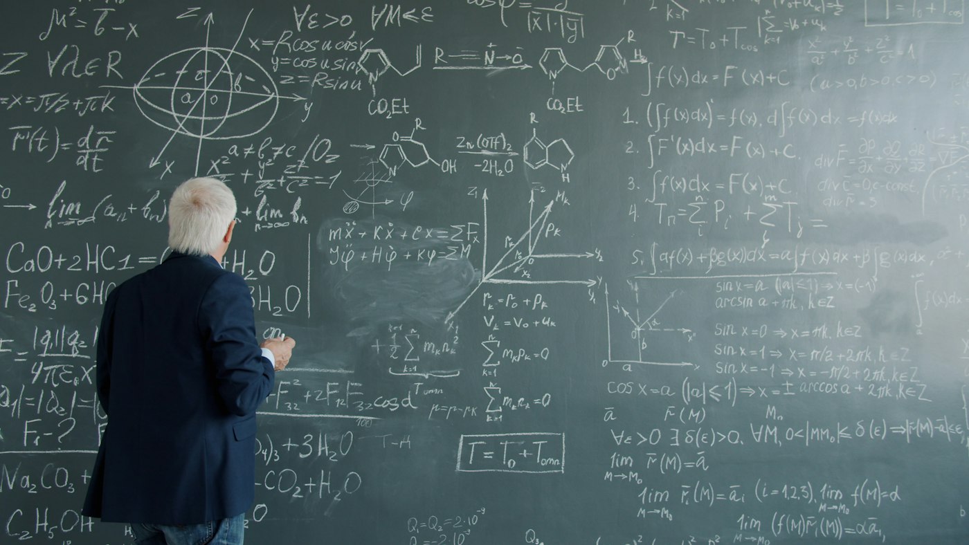 Instructor writing on a chalkboard in front of a lecture hall