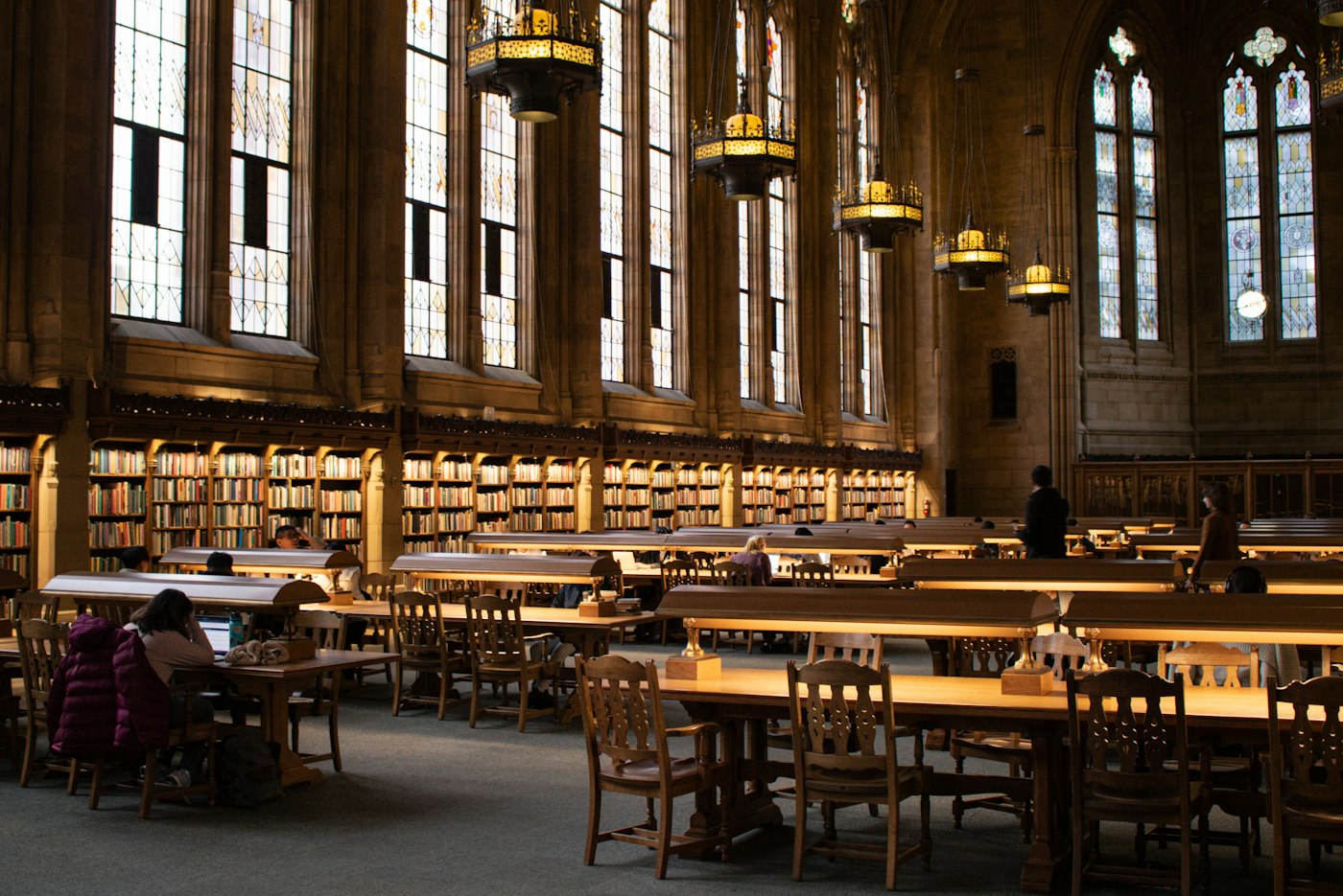 The reading room: long tables and lamp-lit shelves behind tall arched windows