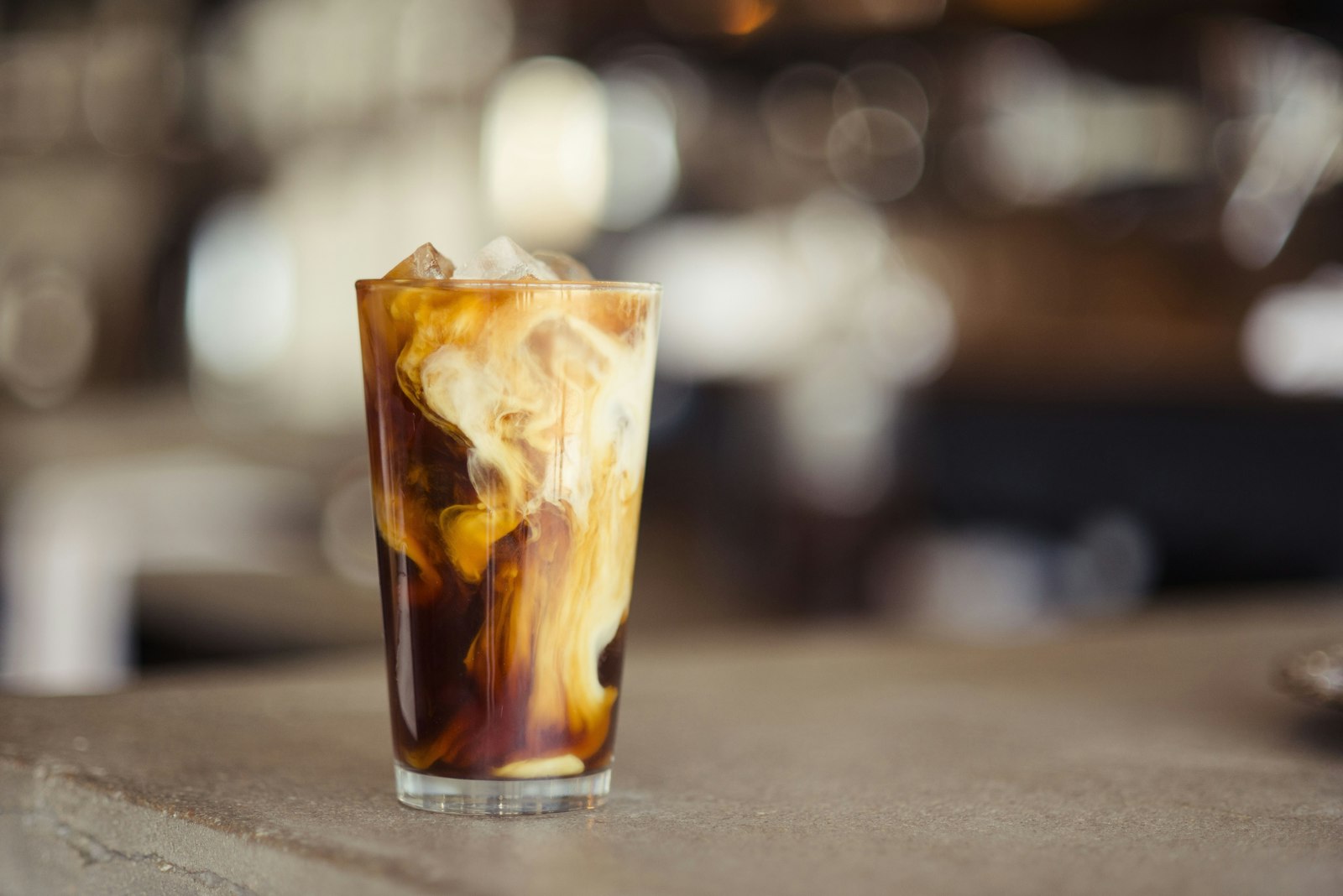 Iced coffee with milk swirling through it on a café counter