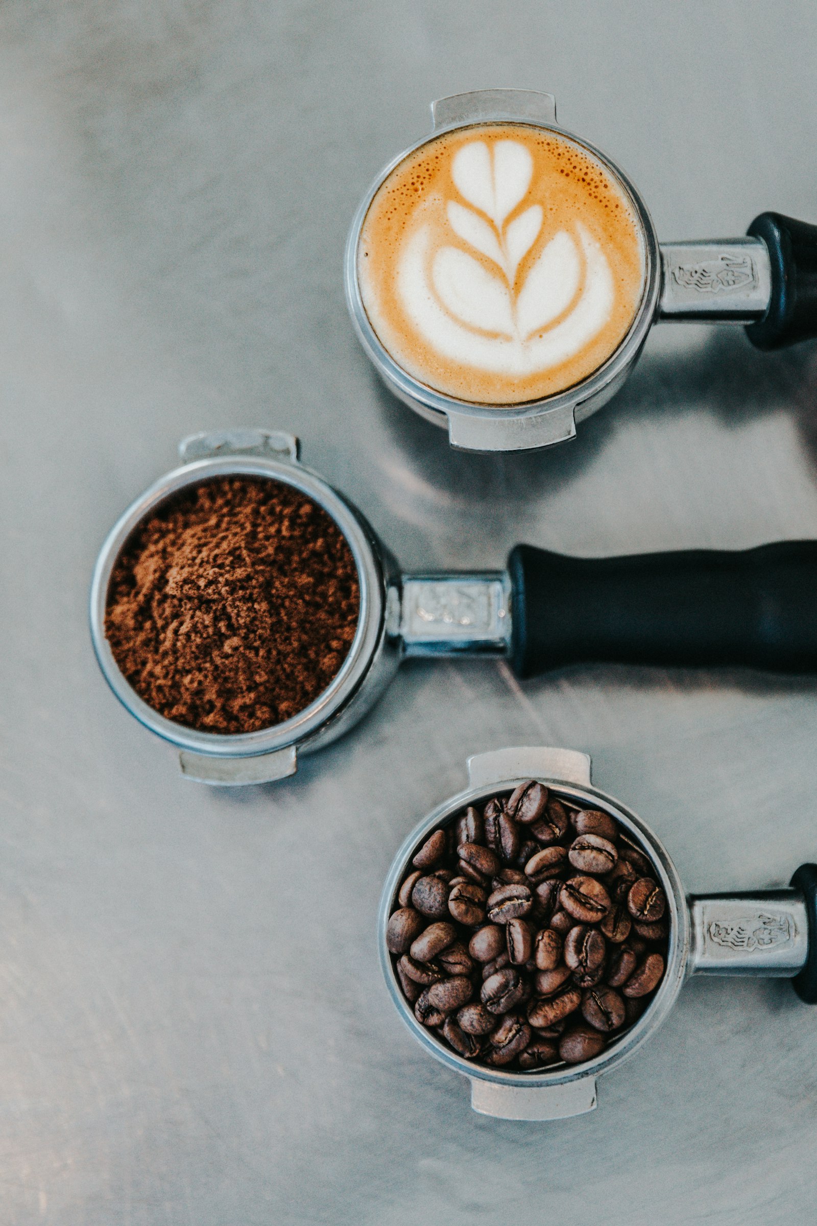 Three portafilters showing whole beans, ground coffee, and a pulled espresso