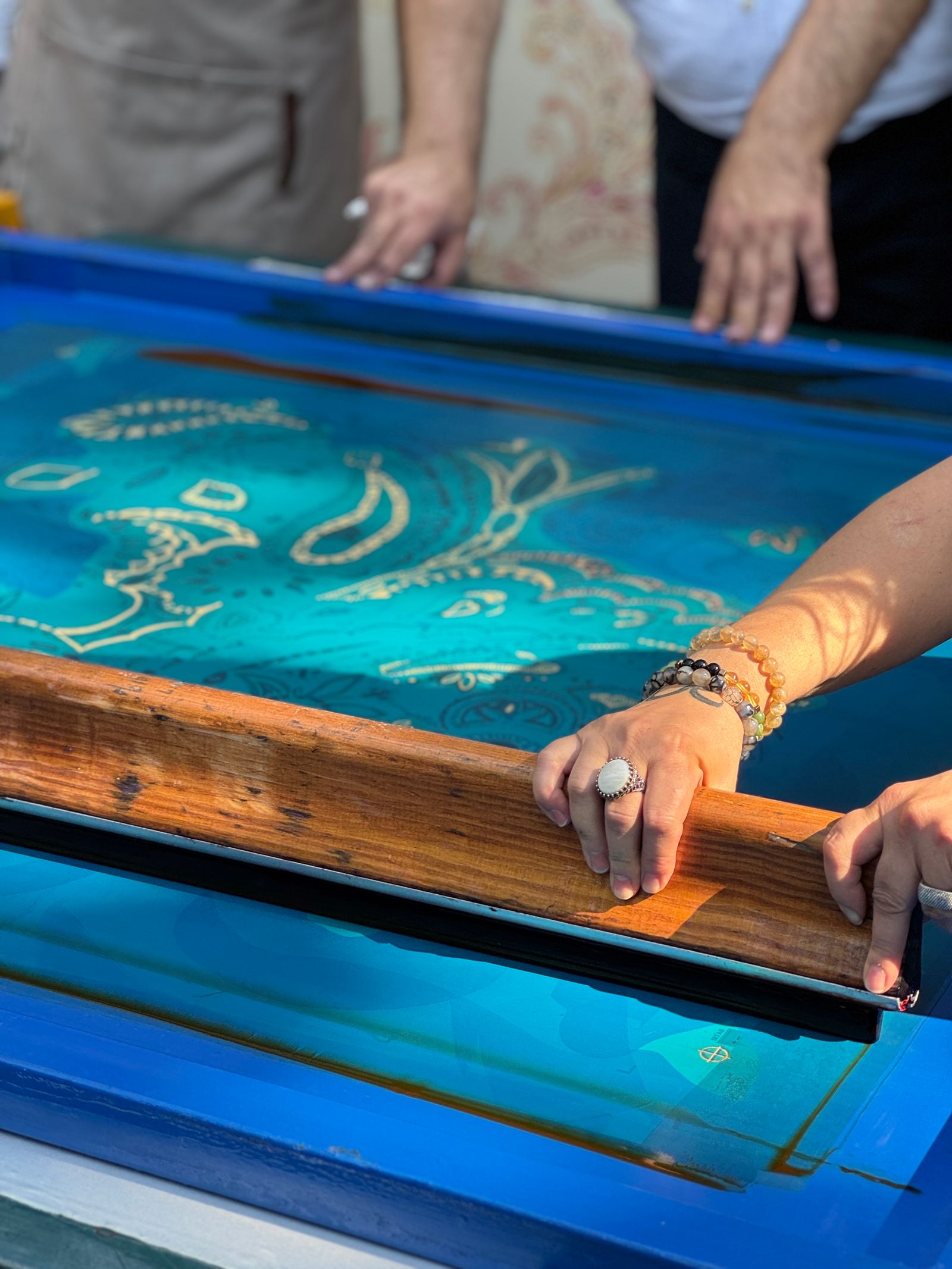 Hands pulling ink across a screen-printing table